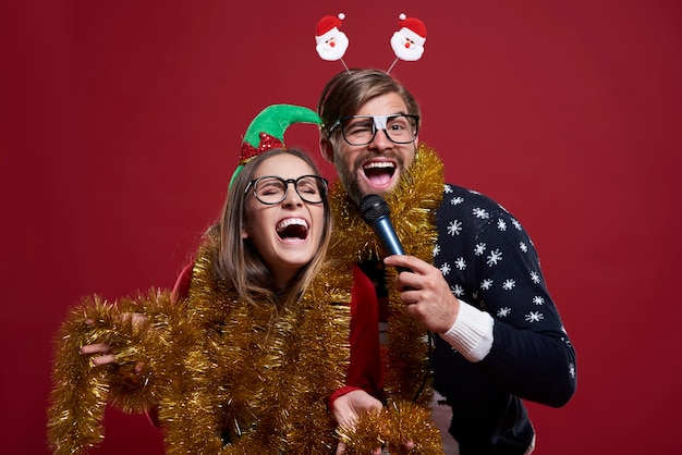 Pareja vistiendo ropa de Navidad se divierte mucho mientras tiene un espectáculo de karaoke