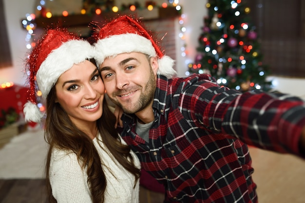 Pareja vistiendo el sombrero de papa noel haciéndose una autofoto