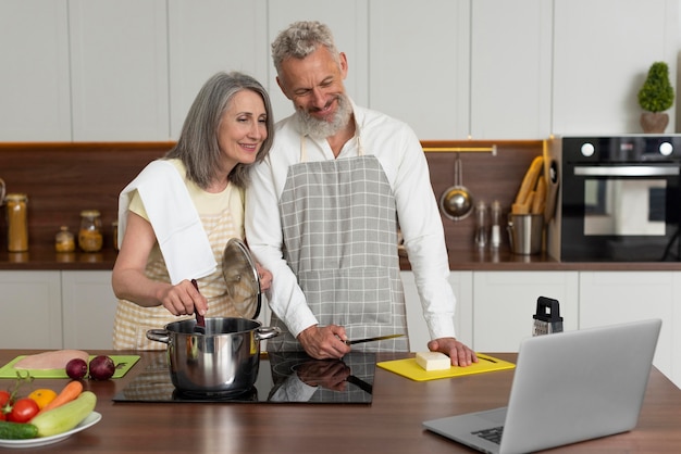 Las parejas ancianas en casa en la cocina tomando lecciones de cocina en el portátil