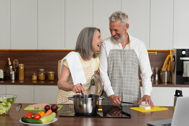 Las parejas ancianas en casa en la cocina tomando lecciones de cocina en el portátil