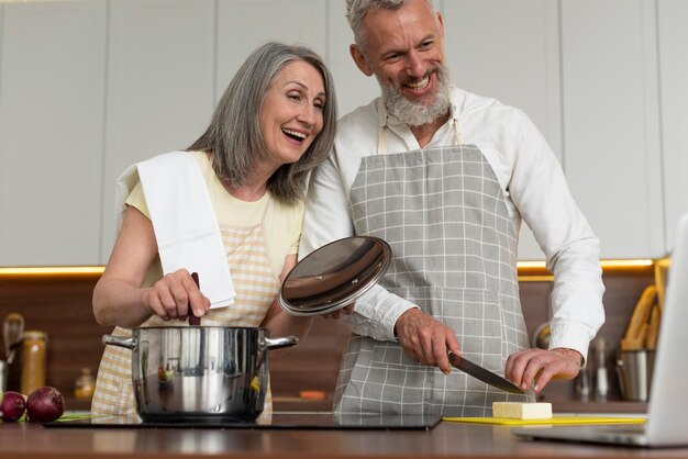 Las parejas ancianas en casa en la cocina tomando lecciones de cocina en el portátil