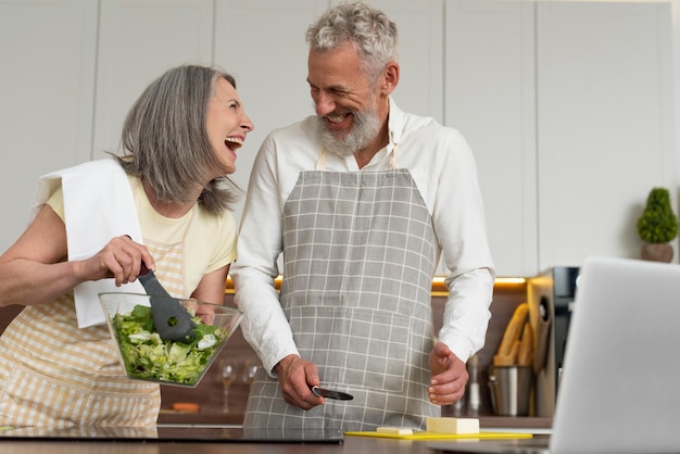 Las parejas ancianas en casa en la cocina tomando lecciones de cocina en el portátil