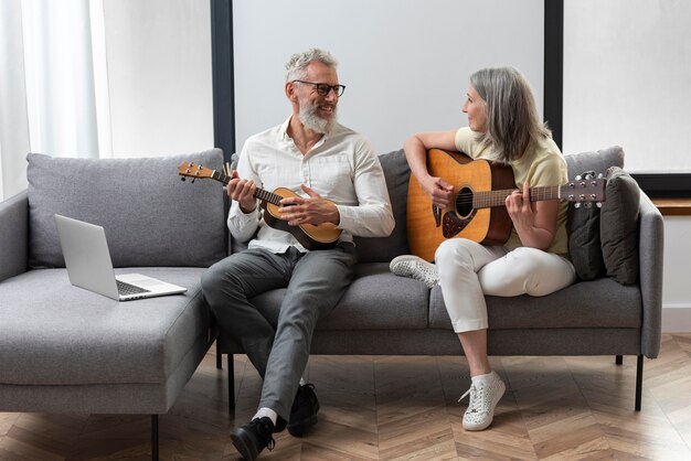 Las parejas ancianas en casa estudiando lecciones de guitarra y ukelele en portátil