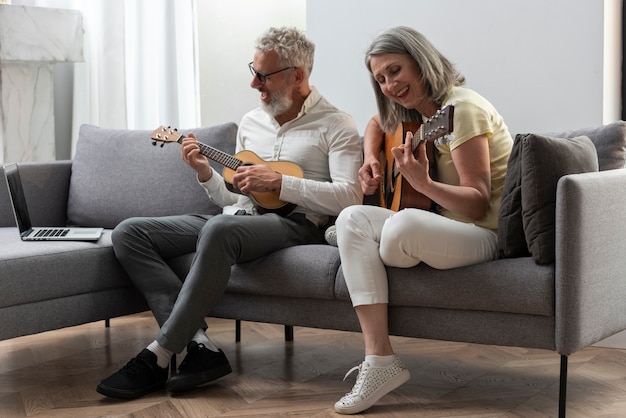 Foto gratuita las parejas ancianas en casa estudiando lecciones de guitarra y ukelele en portátil