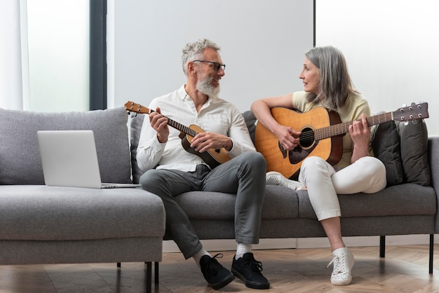 Las parejas ancianas en casa estudiando lecciones de guitarra y ukelele en portátil