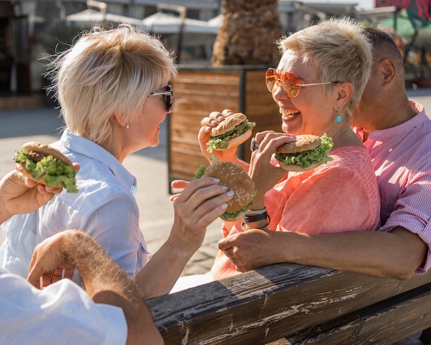 Foto gratuita parejas de ancianos disfrutando de hamburguesas en la playa