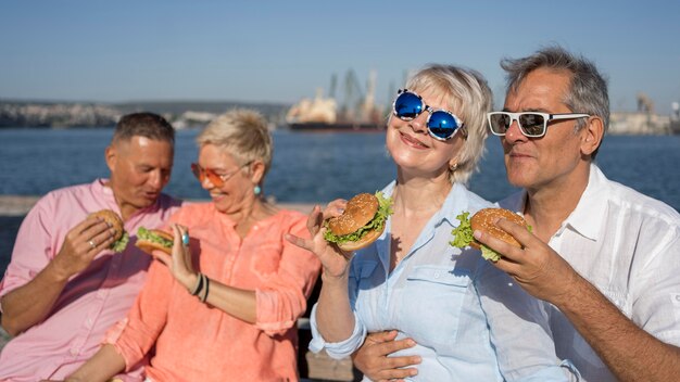 Las parejas mayores en la playa comiendo hamburguesas juntos