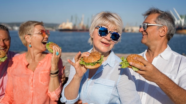 Parejas mayores en la playa disfrutando de hamburguesas juntos