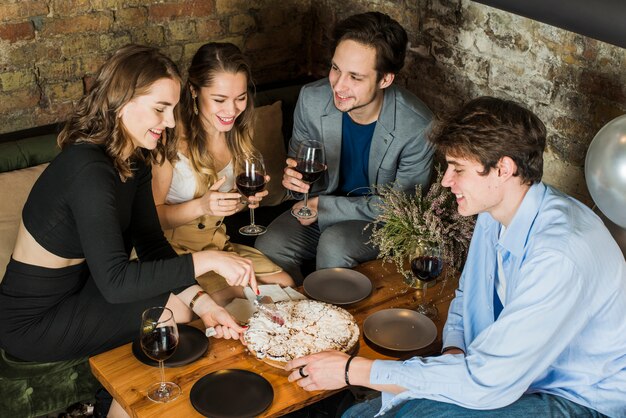 Parejas sonrientes disfrutando de fiesta con pizza y vino.