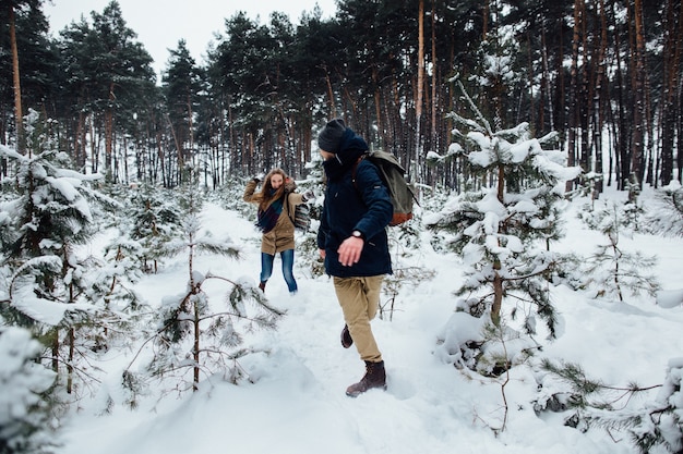 Los pares en el amor se divierten y juegan a la bola de nieve en el bosque de pinos nevados