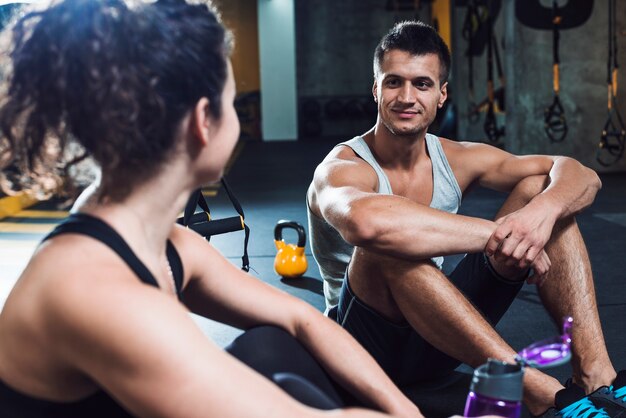 Pares aptos que se sientan en piso en gimnasio