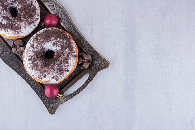 Pares de conos de ciprés, donas y adornos navideños en un plato sobre fondo blanco.