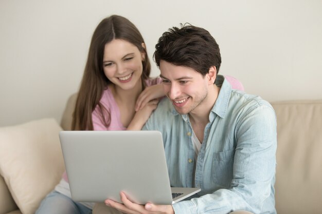 Pares felices jovenes que se sientan usando el ordenador portátil