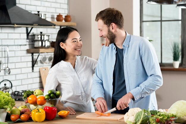 Pares felices que se miran mientras que corta zanahorias en la tajadera