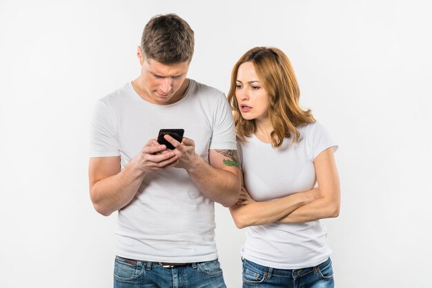 Pares jovenes ansiosos que miran el teléfono móvil contra el contexto blanco
