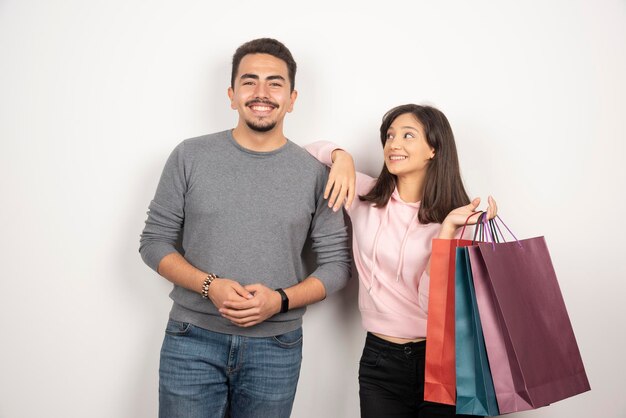 Pares jovenes con los bolsos de compras que se colocan en blanco.