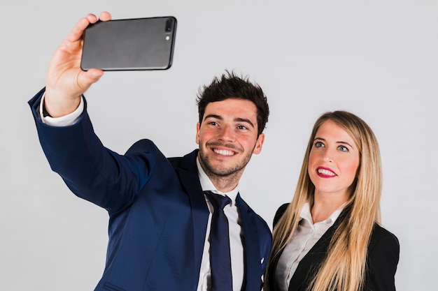 Pares jovenes en el desgaste formal que toma el selfie en smartphone en fondo gris