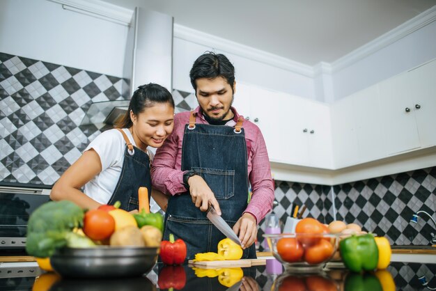 Los pares jovenes felices se ayudan mutuamente cortando la preparación vegetal para cocinar en cocina