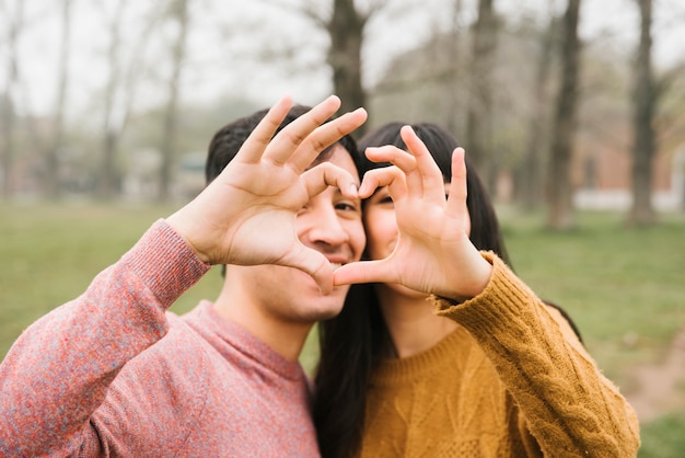 Pares jovenes felices que abrazan mostrando la muestra del corazón