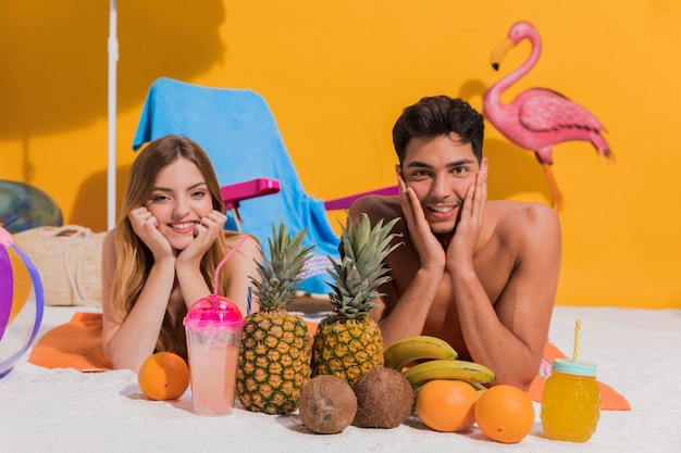 Pares jovenes felices que mienten con la fruta en la playa en estudio