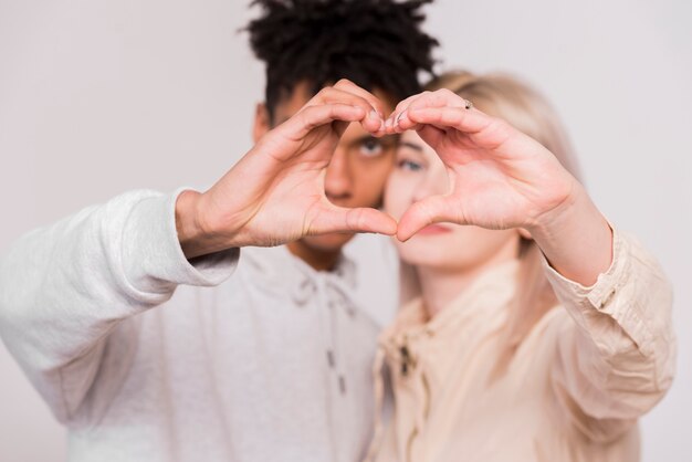 Los pares jovenes interraciales que hacen el corazón forman con las manos aisladas en el fondo blanco