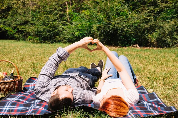 Pares jovenes que mienten en la manta que hace forma del corazón con las manos en el parque