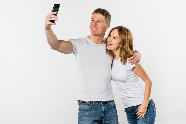 Pares jovenes que toman el selfie en el teléfono móvil aislado en el fondo blanco