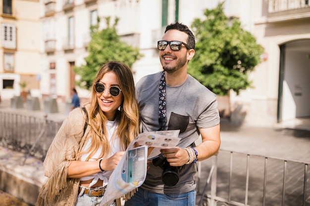 Pares jovenes sonrientes que se colocan en la calle que sostiene el mapa