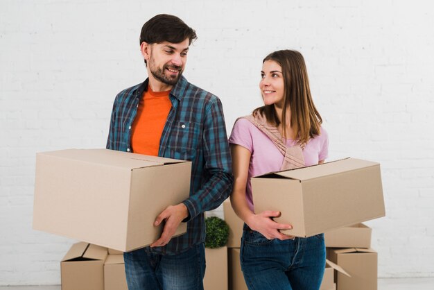 Pares jovenes sonrientes que sostienen las cajas de cartón en la mano que mira uno a