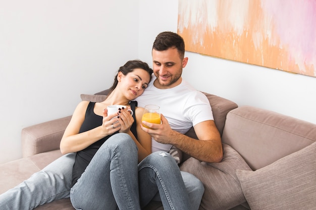 Foto gratuita pares jovenes sonrientes que sostienen la taza de café y el vidrio del jugo en el sofá