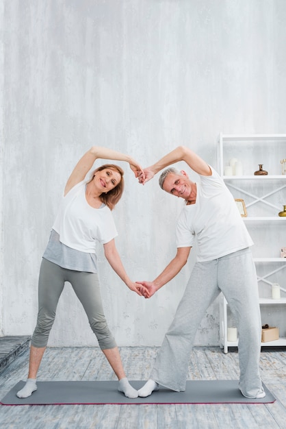 Pares mayores alegres que hacen forma del corazón con sus manos mientras que ejercita en casa