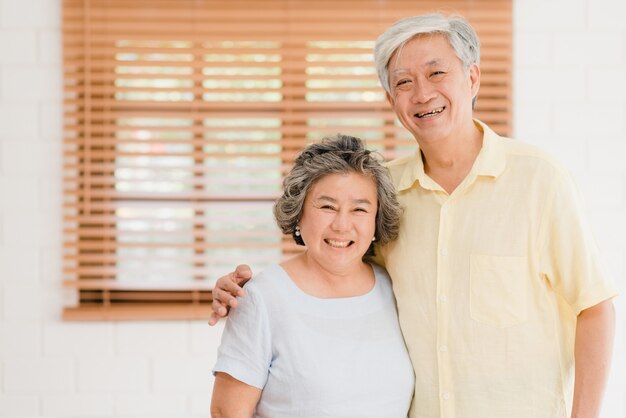 Pares mayores asiáticos que sienten la sonrisa feliz y que miran a la cámara mientras que relájese en sala de estar en casa.