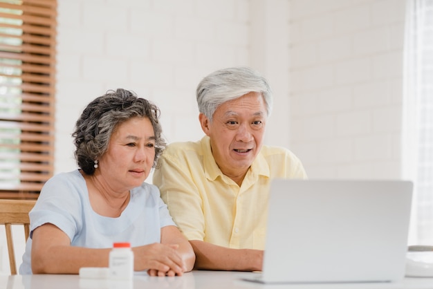 Pares mayores asiáticos que usan conferencia del ordenador portátil con el doctor sobre la información de la medicina en sala de estar