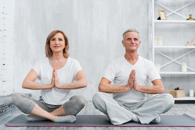 Pares mayores de la familia que se sientan en actitud del loto en la estera gris de la yoga