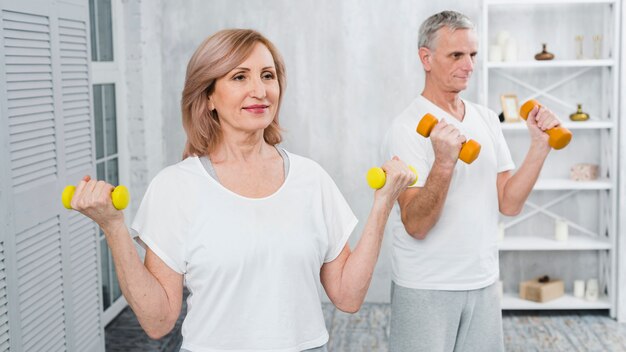 Pares mayores felices que ejercitan usando pesas de gimnasia