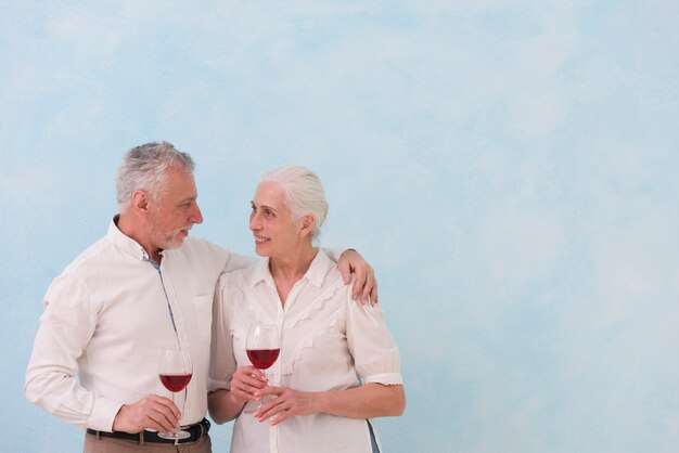 Pares mayores felices que miran uno a que sostiene la copa de vino contra fondo azul