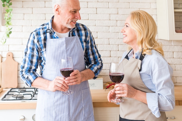 Foto gratuita pares mayores que miran uno a que sostiene las copas de vino disponibles que se colocan en la cocina