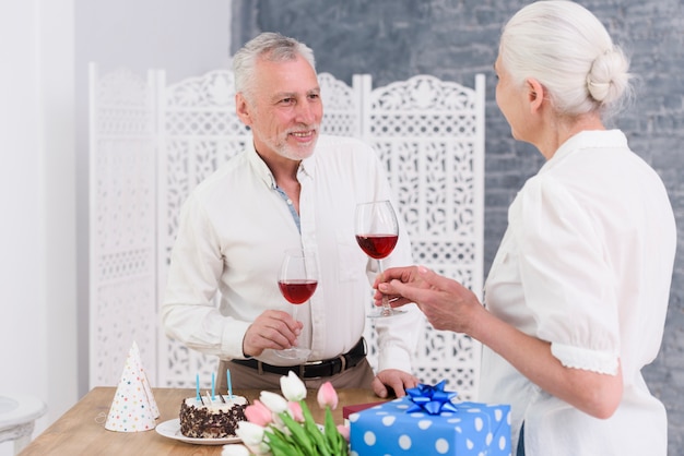 Foto gratuita pares mayores sonrientes que disfrutan de la fiesta de cumpleaños que sostiene las copas de vino rojas disponibles