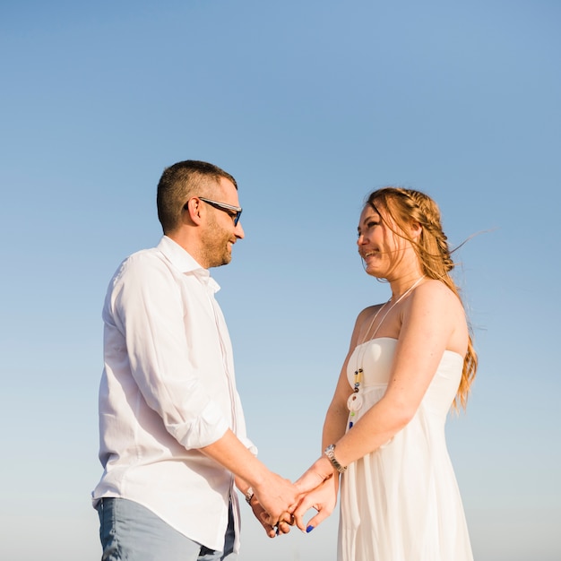 Foto gratuita pares sonrientes que se sostienen la mano de cada uno que está contra el cielo azul