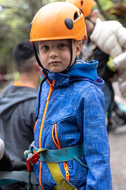 Parque de alta cuerda de escalada de aventuras: niño en curso en casco de montaña y equipo de seguridad