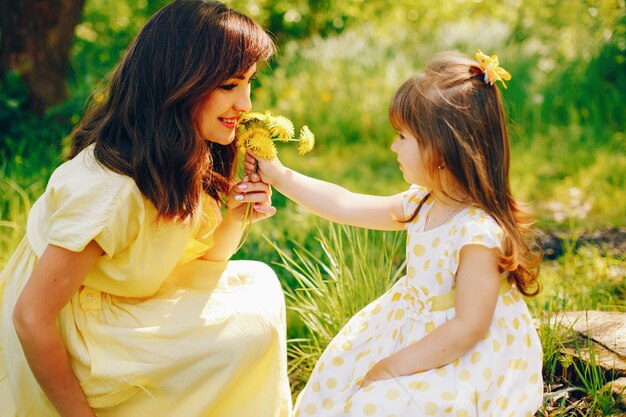 en un parque de verano cerca de árboles verdes, mamá camina vestida de amarillo y su pequeña niña bonita