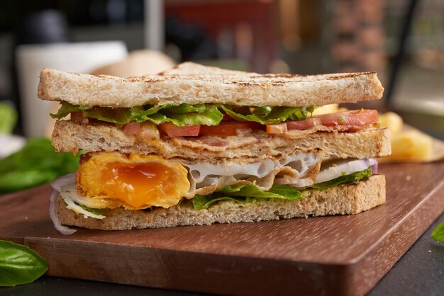 A la parrilla y sándwich con tocino, huevo frito, tomate y lechuga servido en tabla de cortar de madera