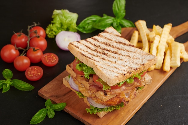 Foto gratuita a la parrilla y sándwich con tocino, huevo frito, tomate y lechuga servido en tabla de cortar de madera