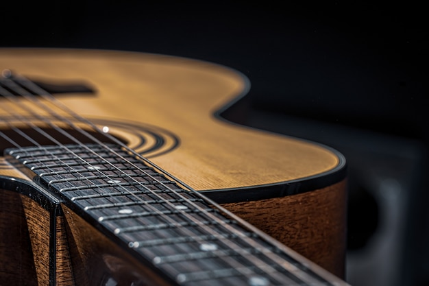 Parte de una guitarra acústica, diapasón de guitarra con cuerdas sobre un fondo negro con reflejos.