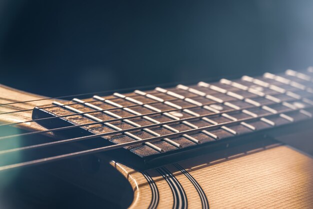 Parte de una guitarra acústica, diapasón de guitarra con cuerdas sobre un fondo negro con reflejos.