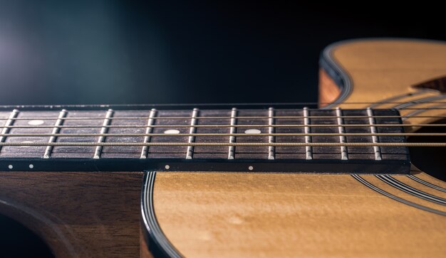 Parte de una guitarra acústica, diapasón de guitarra con cuerdas sobre un fondo negro.