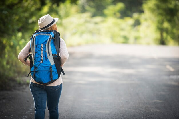 Parte posterior del mochilero de la mujer joven que camina en la trayectoria de bosque y que ve la naturaleza alrededor.