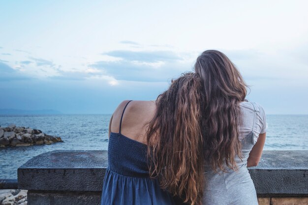 Parte posterior de la mujer apoyada en el hombro de un amigo mirando el mar