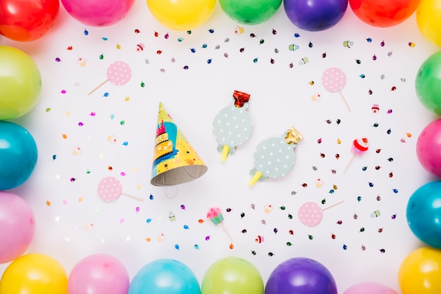 Parte sombrero y soplador de cuerno decorado con globos de colores y confeti aislados sobre fondo blanco