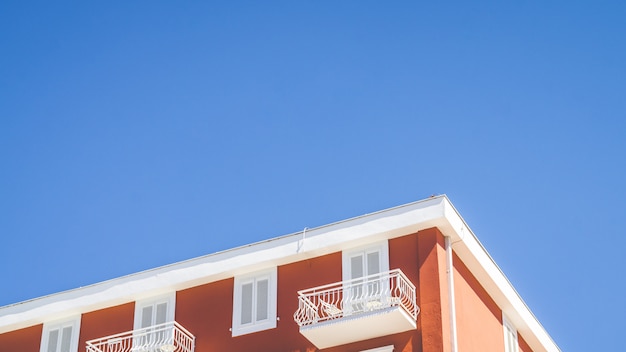 Parte superior de un edificio naranja con un balcón blanco y una ventana con un cielo azul claro en el fondo